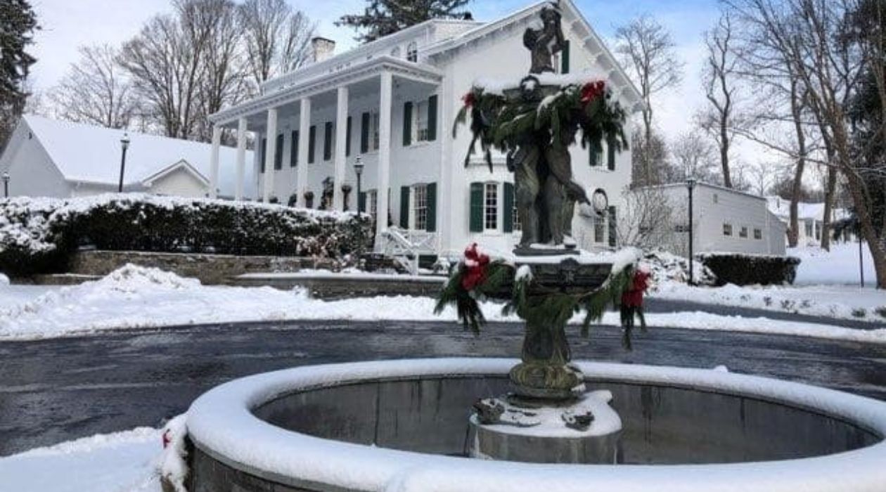 The elegant stone fountain on the grounds of Curry Estate in Hopewell Junction, covered with a dusting of snow and decorated with green evergreen branches and red bows